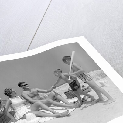 1960s at the beach two boys with baseball bat trying to pull up father seated next to mother so he will play with them by Anonymous