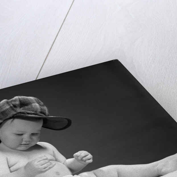 1960s baby in diaper wearing sherlock holmes deerstalker style double-billed cap with magnifying glass resting on leg inspecting a clue by Anonymous