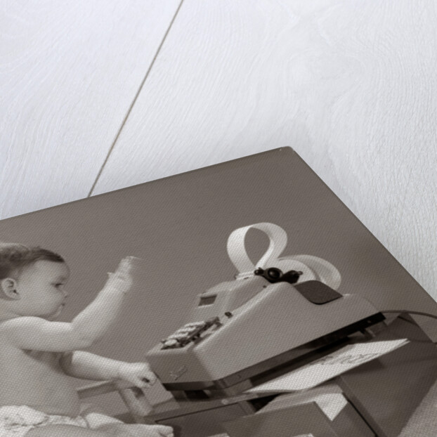 1960s baby seated in small chair hitting keys on office adding machine on top of small file drawers by Anonymous