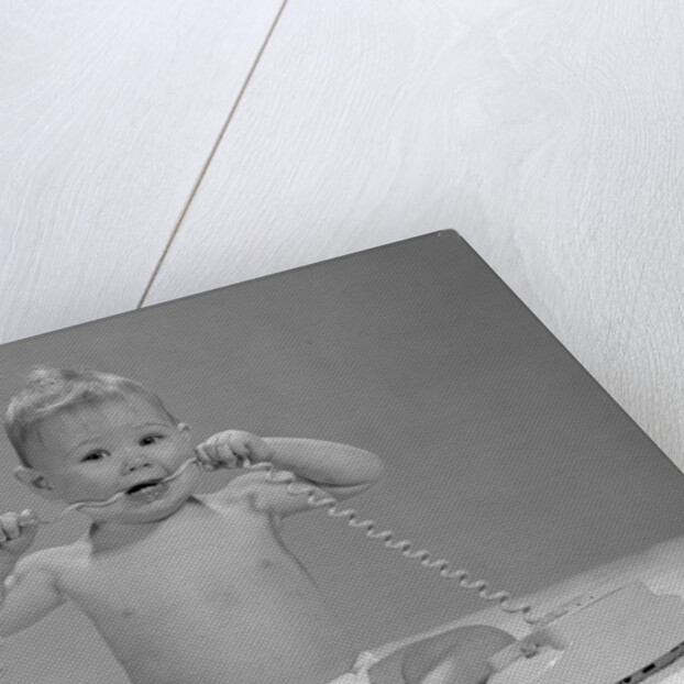 1960s blond baby sitting up looking at camera chewing on telephone cord by Anonymous