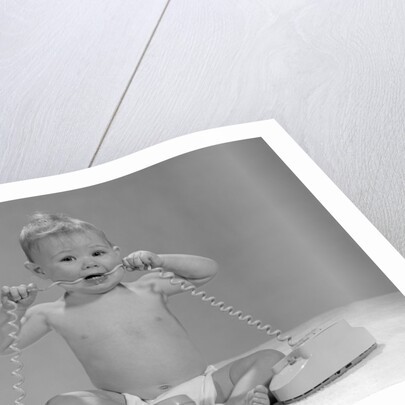 1960s blond baby sitting up looking at camera chewing on telephone cord by Anonymous