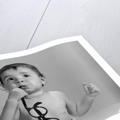 1960s baby in diaper chewing on eyeglasses by Anonymous