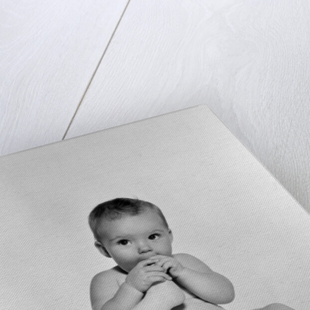 1950s 1960s baby seated on blanket bringing foot to mouth by Anonymous