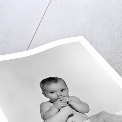 1950s 1960s baby seated on blanket bringing foot to mouth by Anonymous