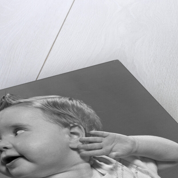 1940s 1950s close-up portrait of baby girl with curl on top of head looking to side with hand held up beside ear by Anonymous