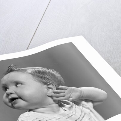 1940s 1950s close-up portrait of baby girl with curl on top of head looking to side with hand held up beside ear by Anonymous