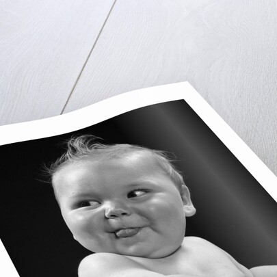 1950s 1940s baby in high chair head turned to one side with tongue sticking out funny facial expression by Anonymous