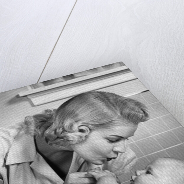 1950s mother woman bending over baby lying on layette holding hands talking by Anonymous