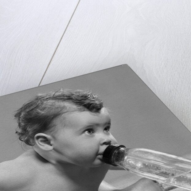 1950s baby sitting leaning forward drinking from bottle studio indoor by Anonymous