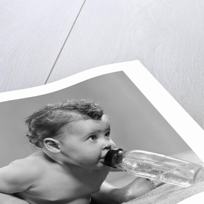 1950s baby sitting leaning forward drinking from bottle studio indoor by Anonymous