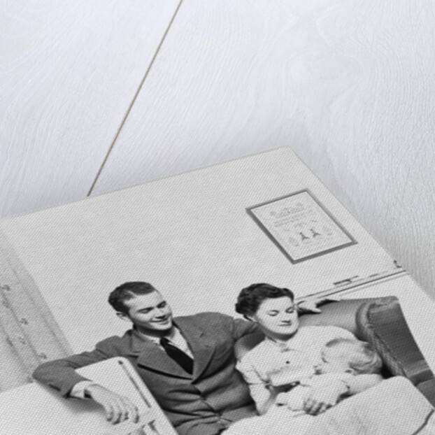 1930s 1940s mother sitting in chair in nursery baby 11 months on lap drinking from bottle father looking on leaning on crib by Anonymous