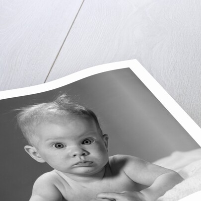 1960s portrait baby lying on stomach with messy hair and bulging eyes looking at camera by Anonymous