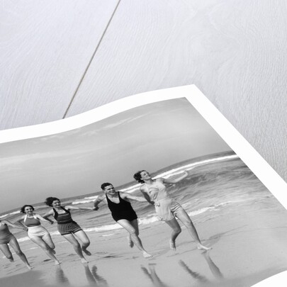 1930s four women and one man running on beach holding hands by Anonymous