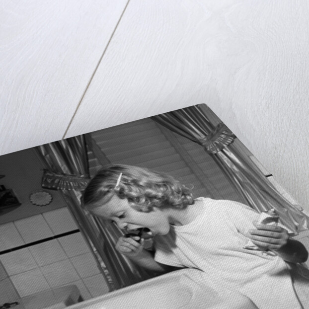 1950s little blond girl in pajamas standing at bathroom sink brushing her teeth toothpaste and toothbrush in hand by Anonymous