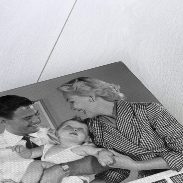 1950s smiling parents picking baby up out of crib by Anonymous