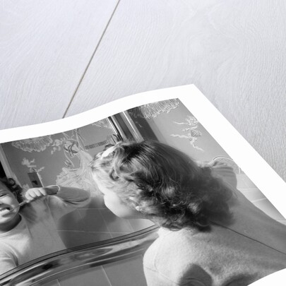 1950s girl looking in bathroom mirror brushing teeth by Anonymous