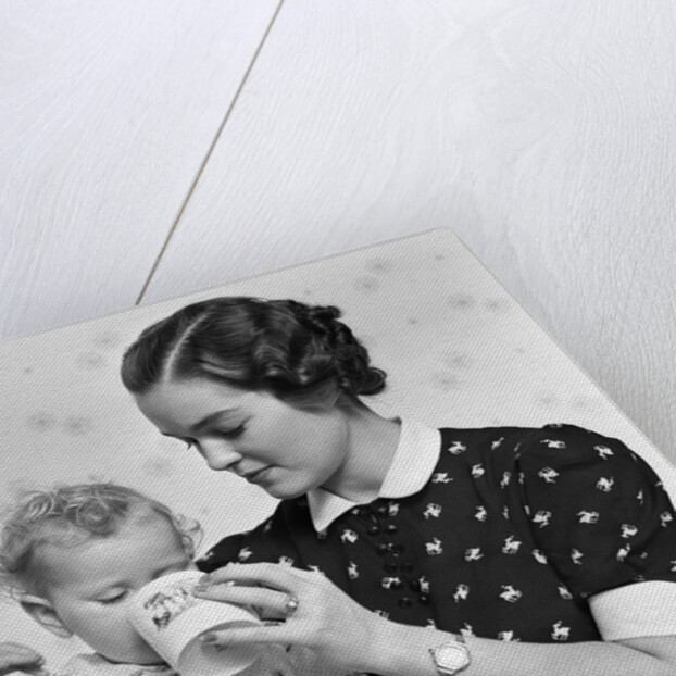 1930s woman mother giving baby daughter drink from mug by Anonymous