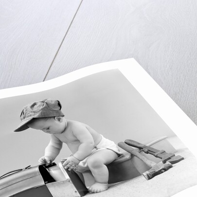 1940s baby in railroad engineer hat pulling milk bottle from lunch pail with hammer & wrench tools at side studio by Anonymous