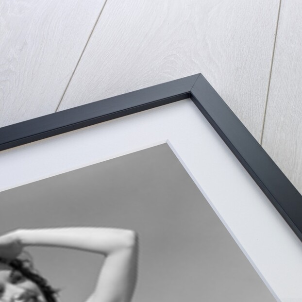 1950s smiling young woman kneeling in grassy sand wearing polka dot bikini shading eyes from sun by Anonymous
