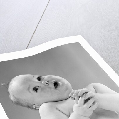 1950s baby in diaper head to one side arms hands clasped in front by Anonymous