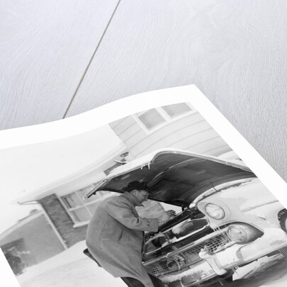 1950s man winter driveway trying to start fix car hood up by Anonymous