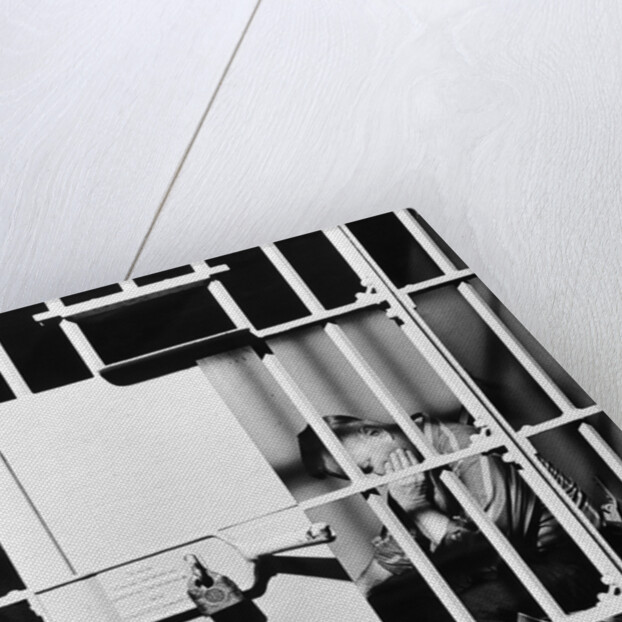 1960s man seated on bench in jail cell with head in hand looking downward by Anonymous