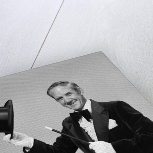 1970s smiling man magician wearing velvet tuxedo white gloves pointing magic wand at top hat looking at camera by Anonymous