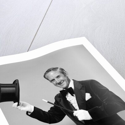 1970s smiling man magician wearing velvet tuxedo white gloves pointing magic wand at top hat looking at camera by Anonymous