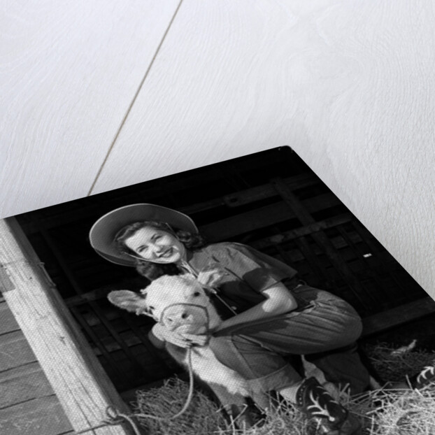 Girl posing with calf in straw filled stall in barn by Anonymous