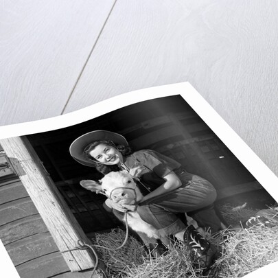Girl posing with calf in straw filled stall in barn by Anonymous