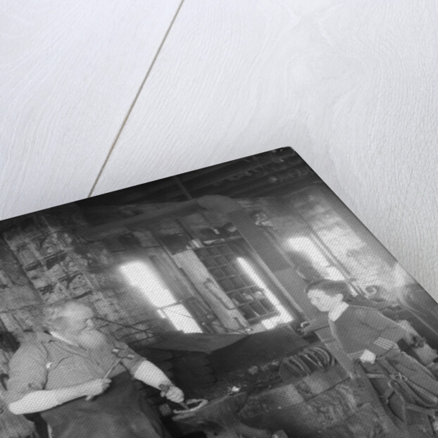 1930s elderly blacksmith with hammer at anvil as young boy holding harness looks on smiling by Anonymous