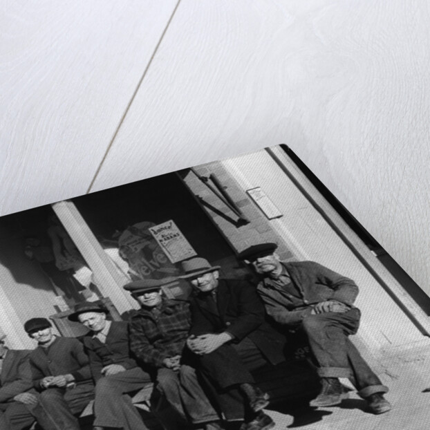 1920s 1930s group of old men in hats & dungarees sitting on bench in front of store window looking at camera by Anonymous