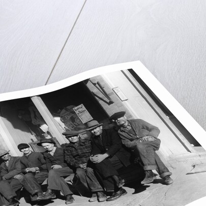 1920s 1930s group of old men in hats & dungarees sitting on bench in front of store window looking at camera by Anonymous