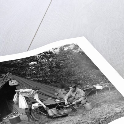 1920s couple man woman on fishing camping trip vacation at campsite man cooking over fire by Anonymous