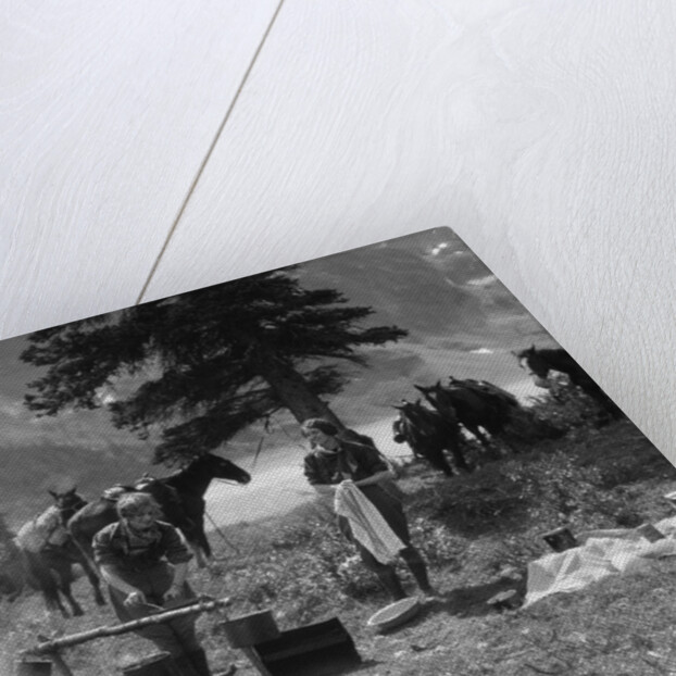 1920s 1930s two women at campsite woman cooking preparing food over campfire horses with riding gear in background by Anonymous