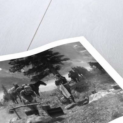 1920s 1930s two women at campsite woman cooking preparing food over campfire horses with riding gear in background by Anonymous
