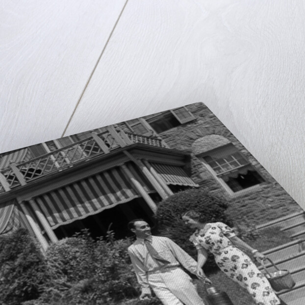 1930s couple walking out of house down sidewalk carrying picnic baskets & thermos jug by Anonymous