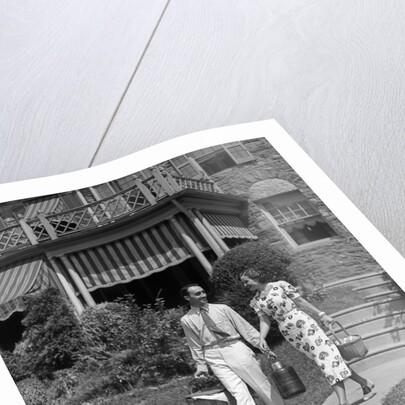 1930s couple walking out of house down sidewalk carrying picnic baskets & thermos jug by Anonymous