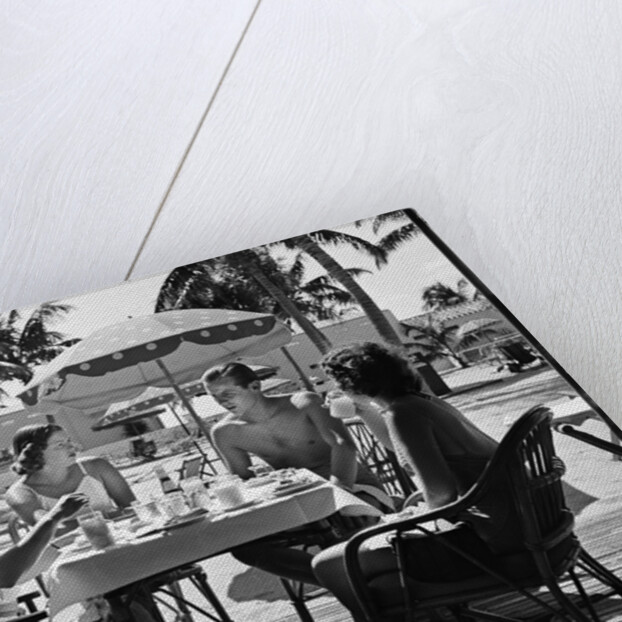 1930s three women and one man sitting at tropical pool side table talking together by Anonymous