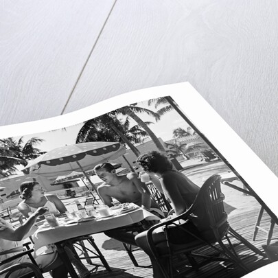 1930s three women and one man sitting at tropical pool side table talking together by Anonymous