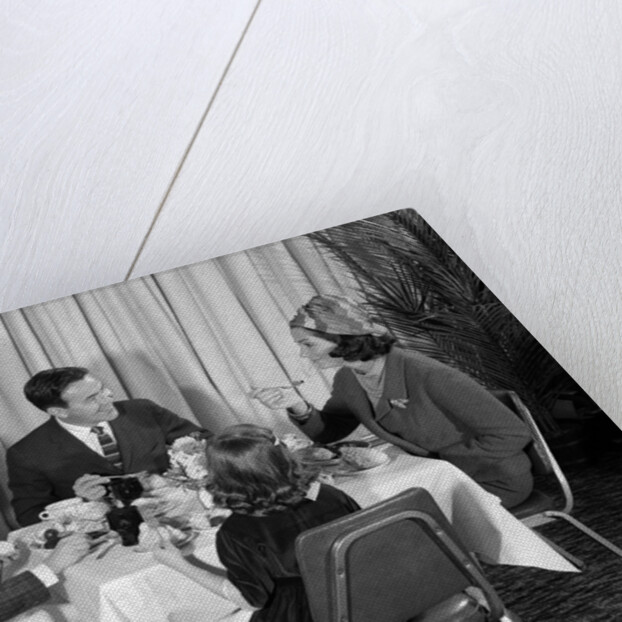 1960s smiling happy family of four eating meal in restaurant dad talking to mom who is wearing turban style hat by Anonymous