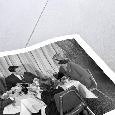 1960s smiling happy family of four eating meal in restaurant dad talking to mom who is wearing turban style hat by Anonymous