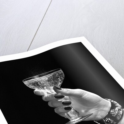 1930s 1940s 1950s woman hand ornate metal bracelet holding up new year toast glass of champagne against black background by Anonymous