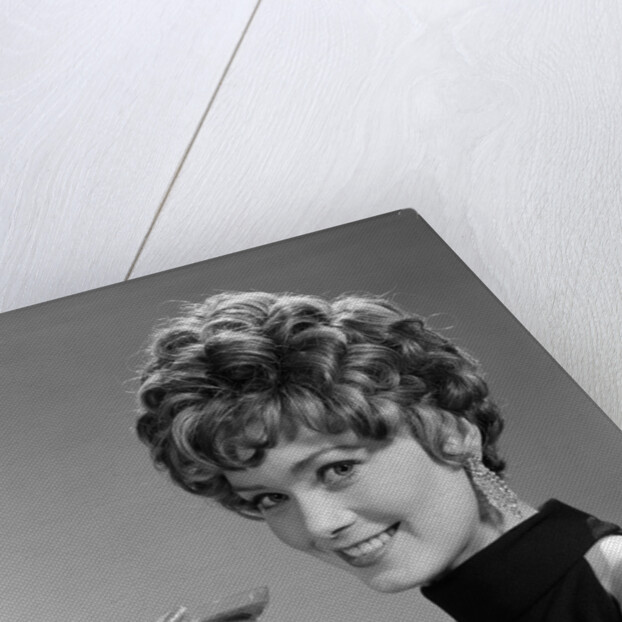 1960s glamorous woman with curly hair and dangling earrings smiling holding a champagne glass looking at camera by Anonymous