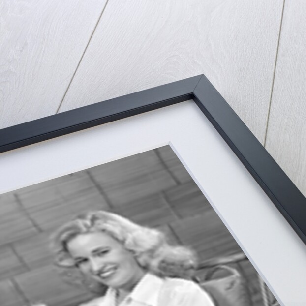 1940s blonde woman in bamboo chair holding up glass of milk smiling wearing white shorts looking at camera by Anonymous