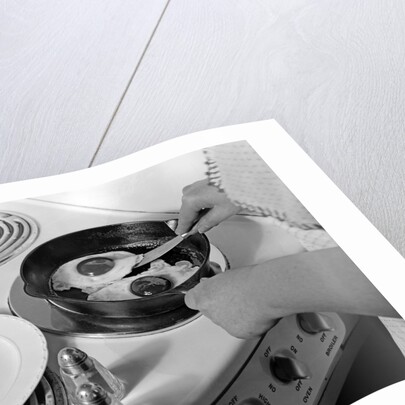 1940s 1950s woman hands frying eggs in iron skillet on electric stove salt and pepper shakers by Anonymous