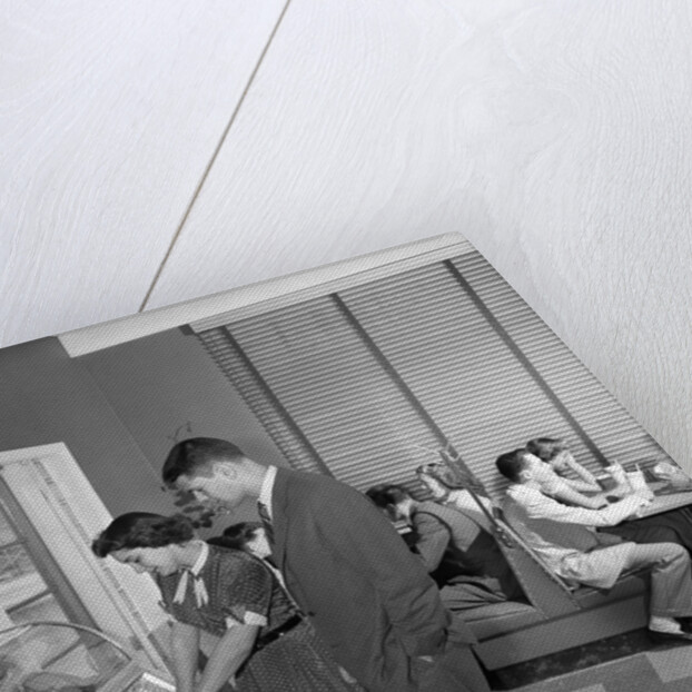 1950s teen couple playing juke box in malt shop with other teens in booths by Anonymous