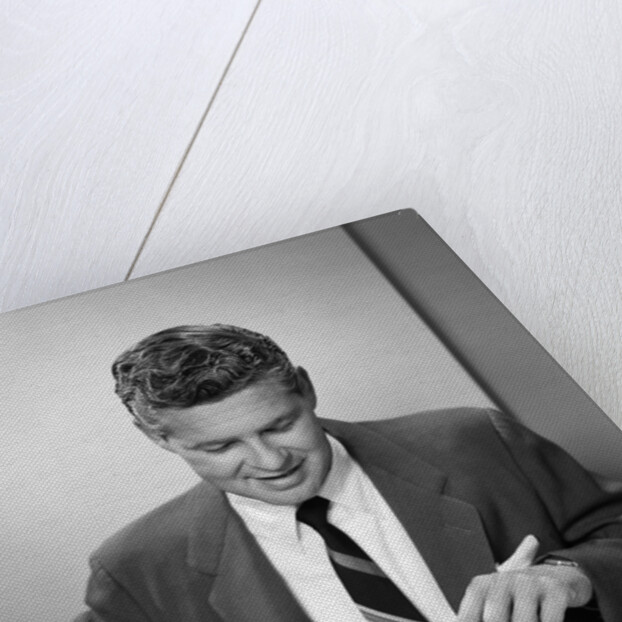 1950s smiling man in suit and tie sitting at table holding knife and fork eating dinner by Anonymous