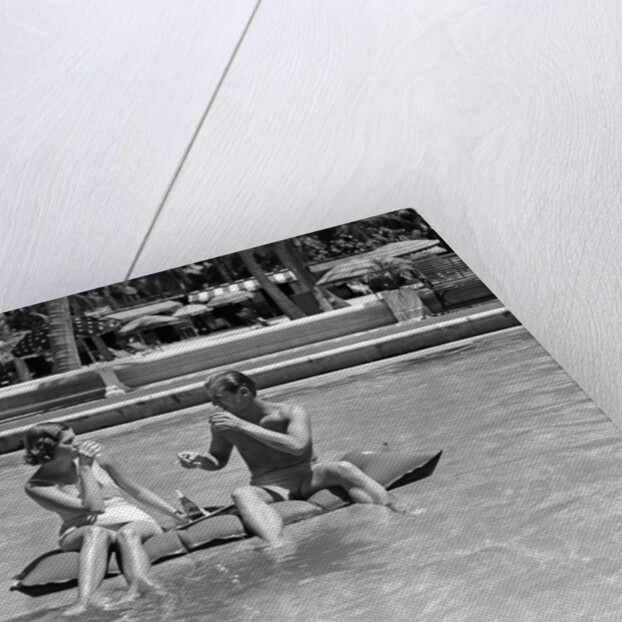 1930s 1940s couple drinking while floating in a pool on a rubber raft at florida resort by Anonymous