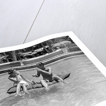 1930s 1940s couple drinking while floating in a pool on a rubber raft at florida resort by Anonymous
